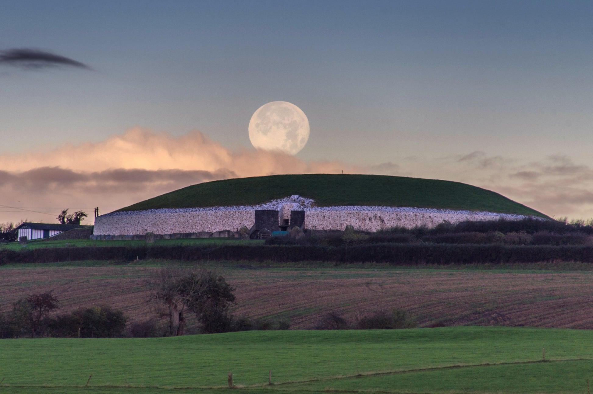 The full moon in winter time sets behind Newgrange as viewed from the south bank of the river Boyne